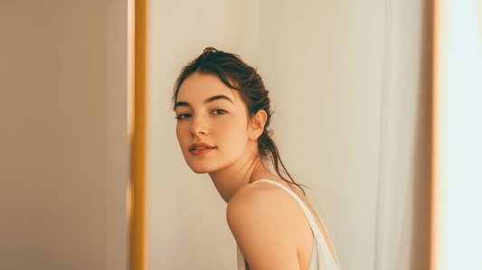 Confident young woman in her 20s with smooth, glowing skin, looking at herself in the mirror in a softly lit, modern bathroom. The image conveys natural beauty, self-care, and skincare wellness, ideal for a blog about preventative Botox.