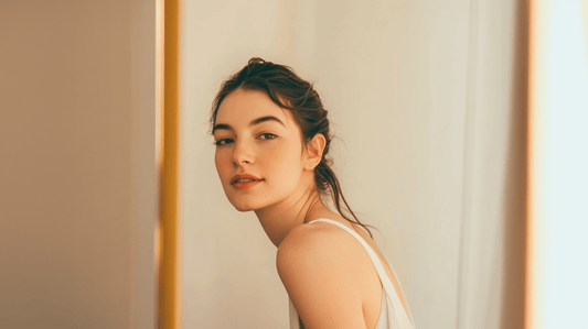 Confident young woman in her 20s with smooth, glowing skin, looking at herself in the mirror in a softly lit, modern bathroom. The image conveys natural beauty, self-care, and skincare wellness, ideal for a blog about preventative Botox.